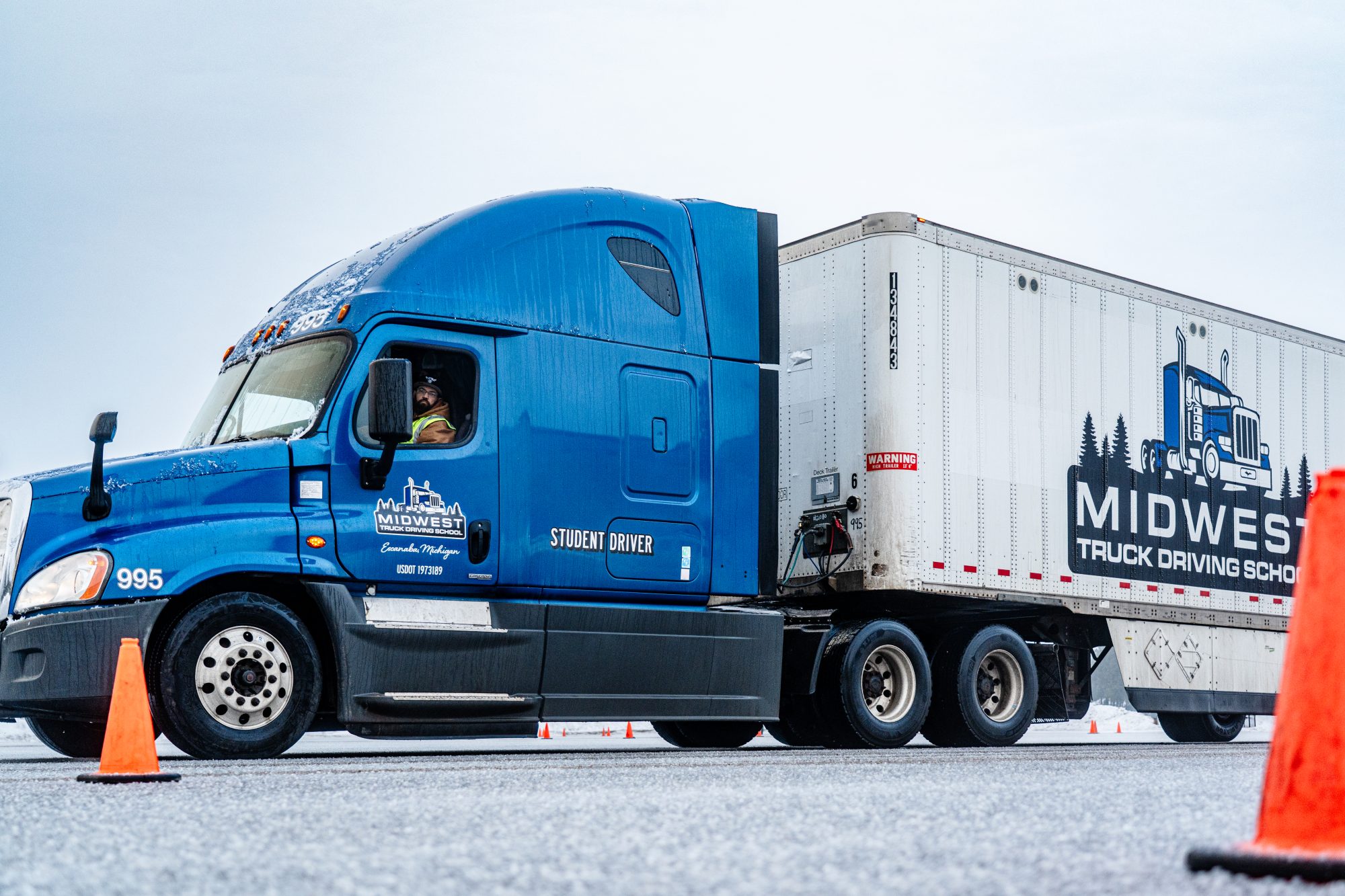 Midwest Truck Driving School student driver behind the wheel of a blue Freightliner semi truck on the training course